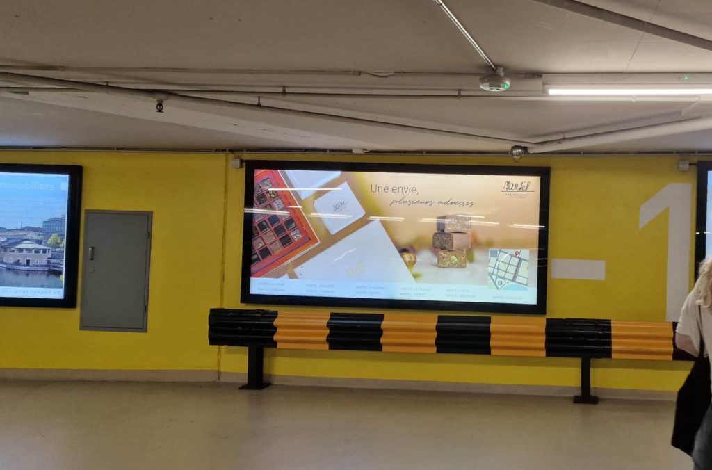 Affiche publicitaire lumineuse au format F12L au parking du Mont-Blanc à Genève, mettant en avant une campagne visuelle élégante pour Martel Chocolatier.