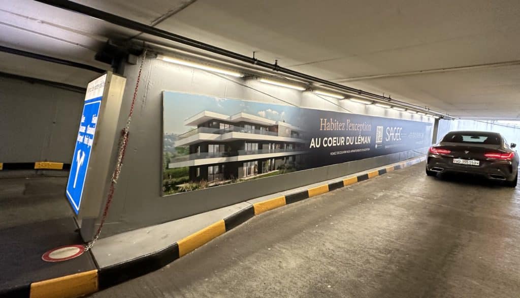 Mégaposter Sagec installé à la sortie Rive Gauche du parking du Mont-Blanc à Genève, présentant le promoteur immobilier et ses projets haut de gamme dans un emplacement urbain stratégique.
