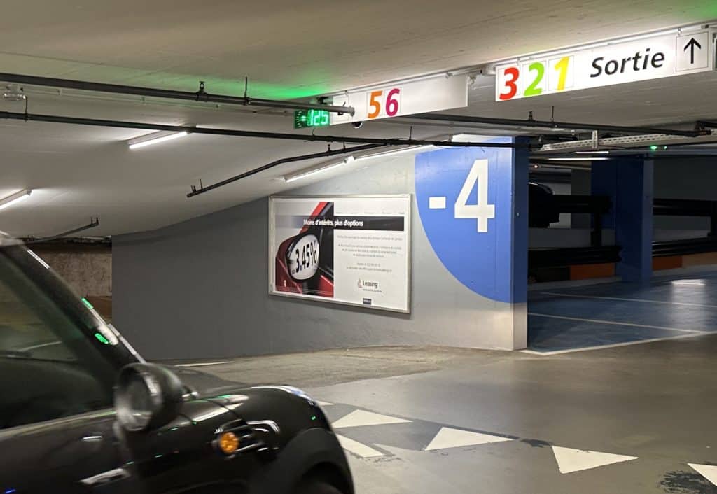 Affiche publicitaire grand format F12 installée au parking de Villereuse à Genève, dans le quartier des Eaux-Vives, offrant une visibilité maximale auprès des automobilistes et piétons.