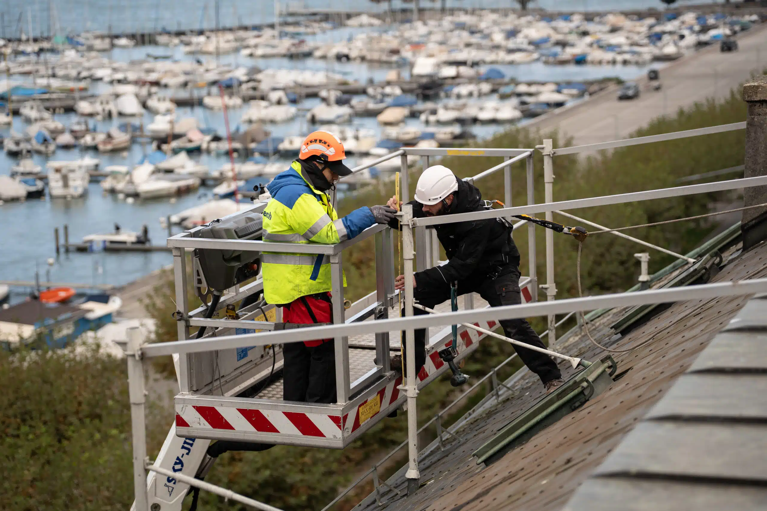 Deux techniciens sur une nacelle installent une enseigne lumineuse connectée à Genève, avec vue sur le lac Léman en arrière-plan