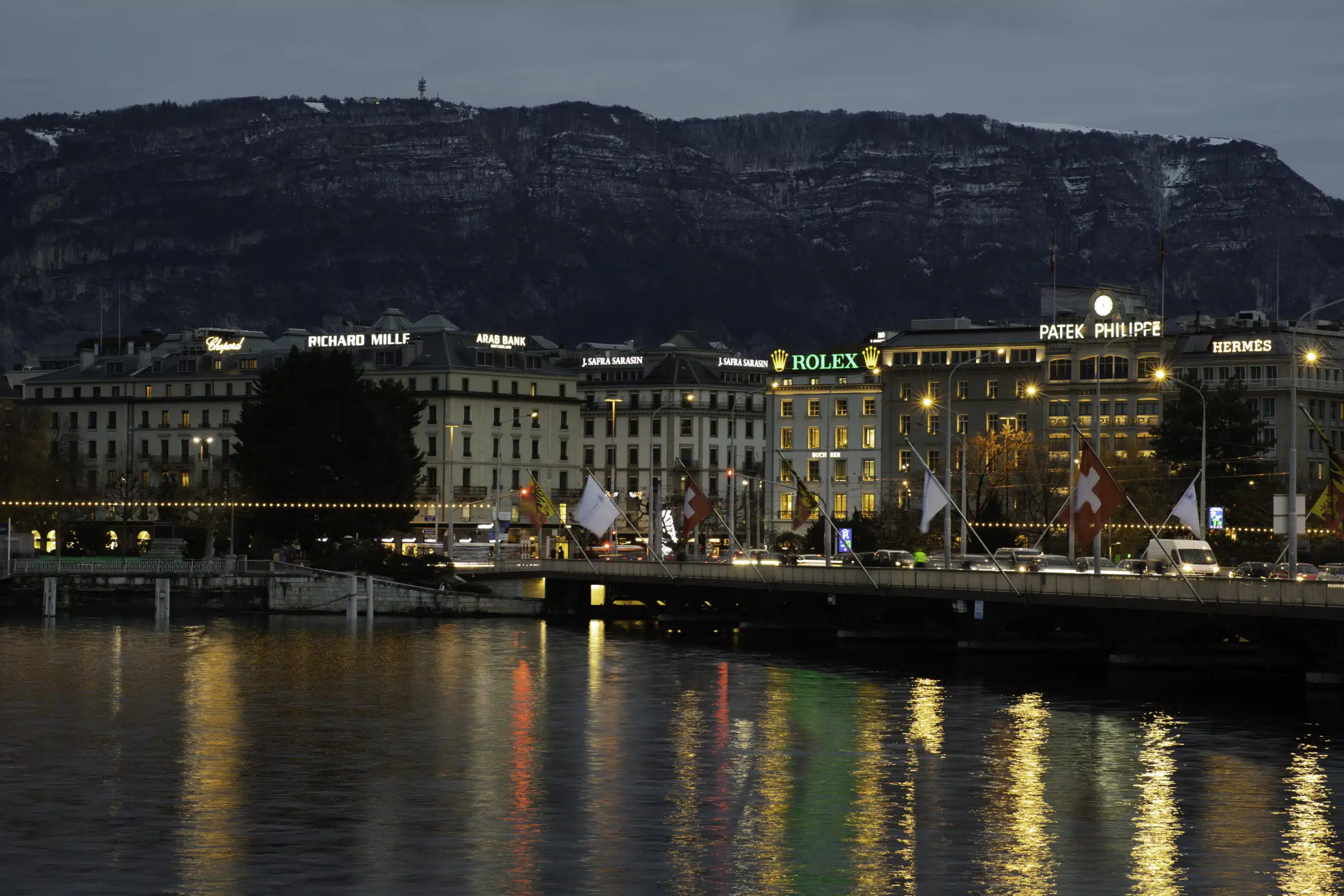 Vue nocturne du pont du Mont-Blanc à Genève avec les enseignes lumineuses des toits visibles en arrière-plan, symbole de la publicité de prestige.