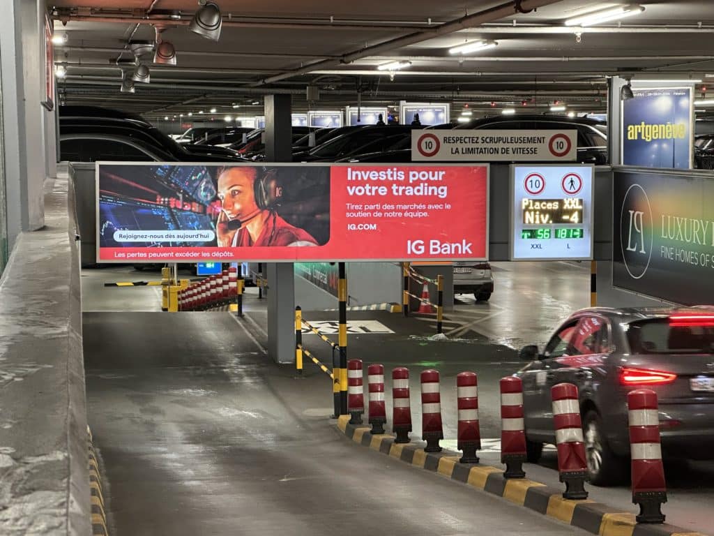 Support publicitaire lumineux positionné en frontal sur les rampes du parking du Mont-Blanc à Genève, utilisé par IG Bank pour renforcer sa visibilité locale.