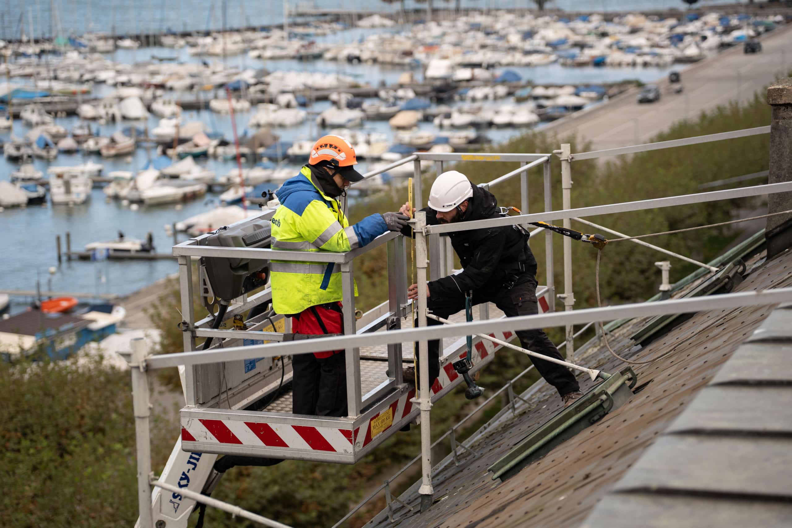 Deux techniciens sur une nacelle installent une enseigne lumineuse connectée à Genève, avec vue sur le lac Léman en arrière-plan