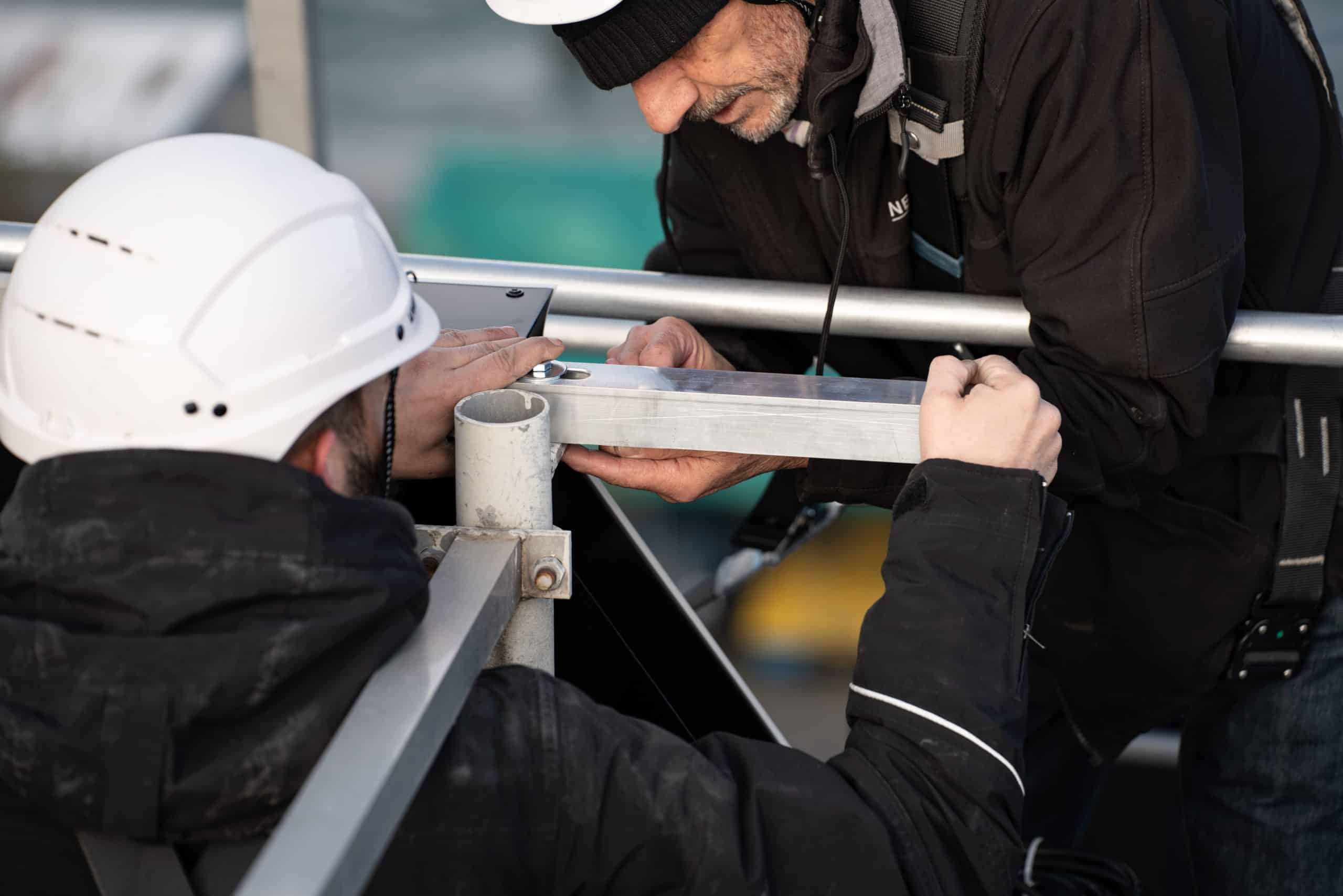 Deux techniciens posent une enseigne lumineuse connectée sur le toit d'un immeuble de la rade de Genève, en assurant un montage précis et sécurisé