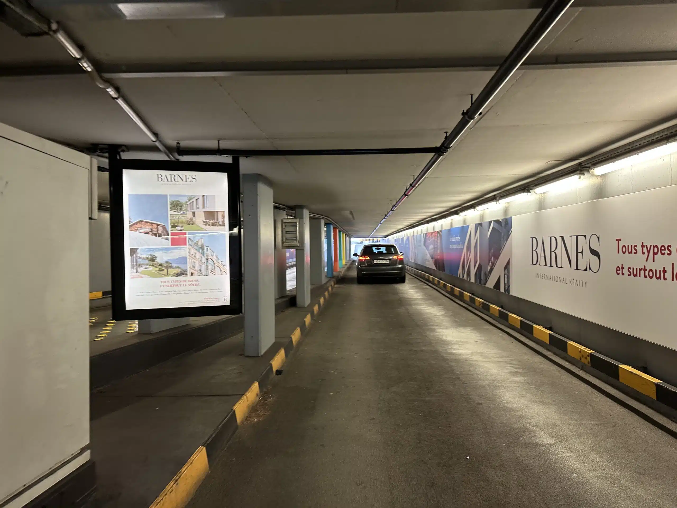 Affichage A0L rétro-éclairé recto-verso BARNES au parking du Mont-Blanc à Genève, mettant en valeur des biens immobiliers de prestige à vendre ou à louer.