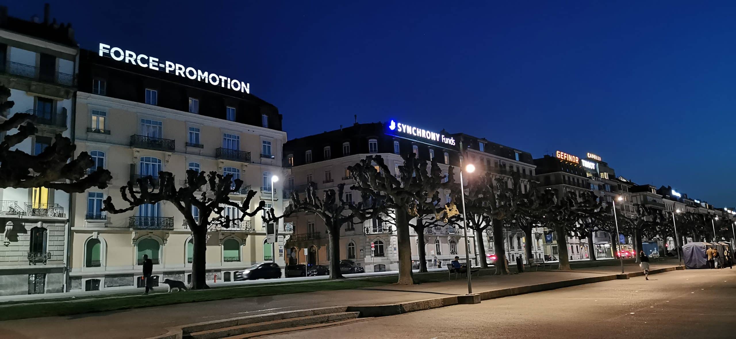Buildings in the centre of Geneva with illuminated signs from Force Promotion lighting up the facades of the buildings