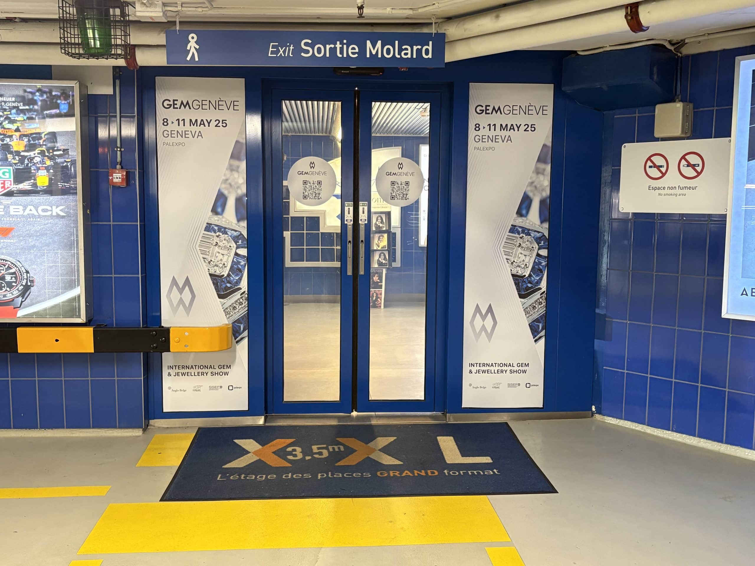 Visuel événementiel GemGenève installé sur les portes coulissantes automatiques du parking du Mont-Blanc à Genève, touchant un public haut de gamme en transit.