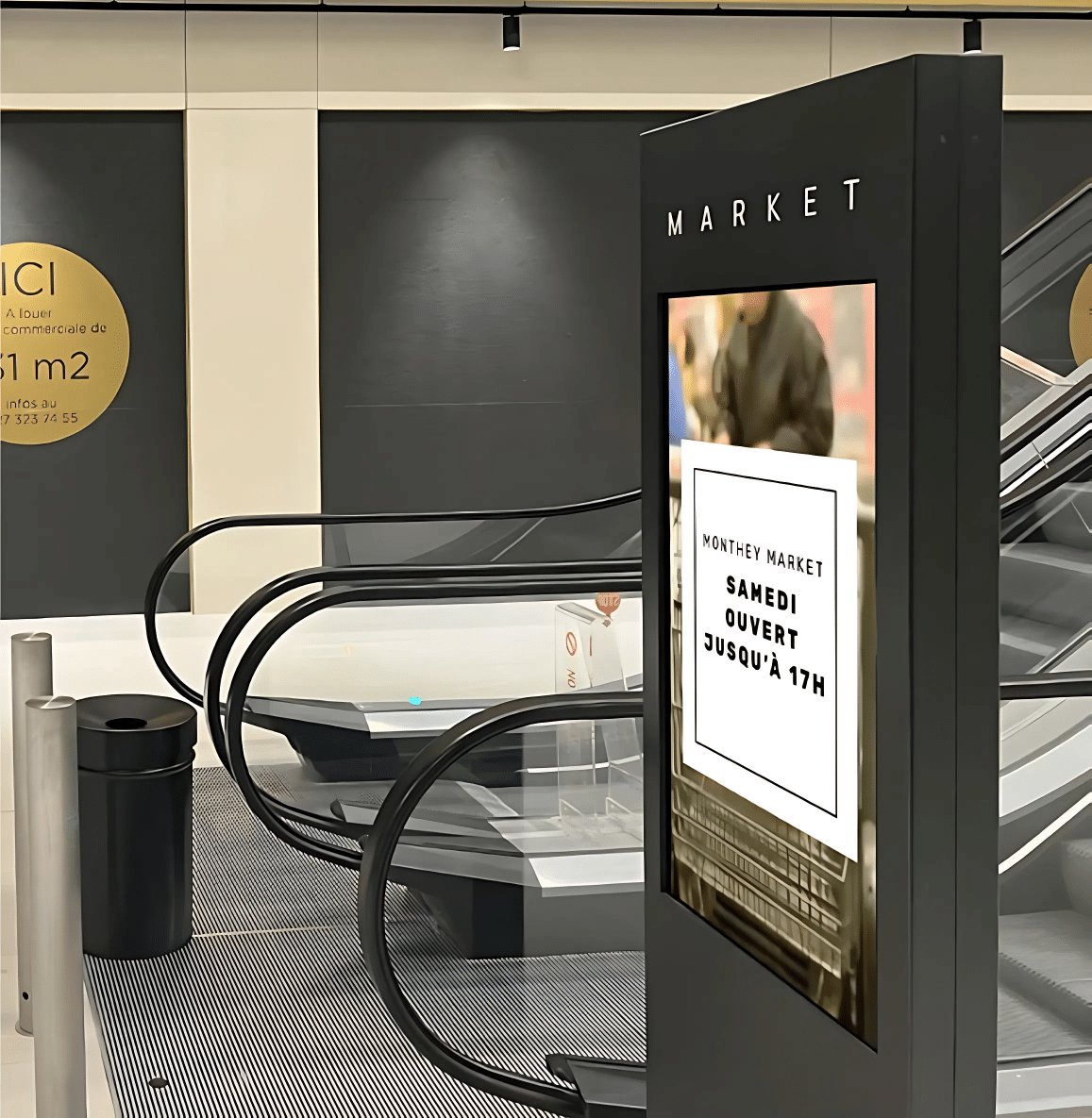 Digital kiosks displaying advertisements on each floor of M Central shopping center in Monthey, visible to visitors moving through the different levels.