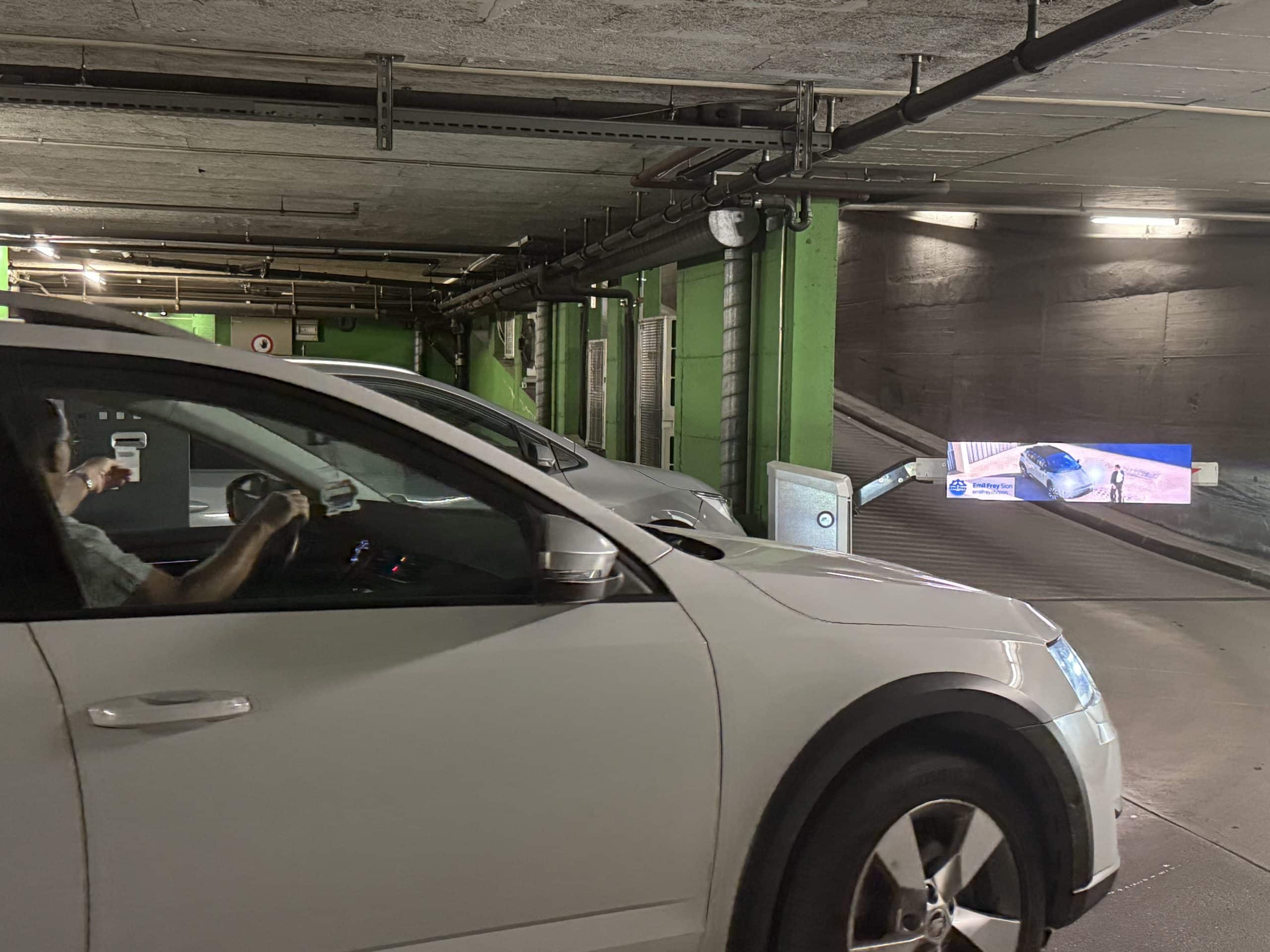 Écrans publicitaires digitaux intégrés aux barrières automatiques du parking Centre Manor à Sion, assurant un impact publicitaire efficace.