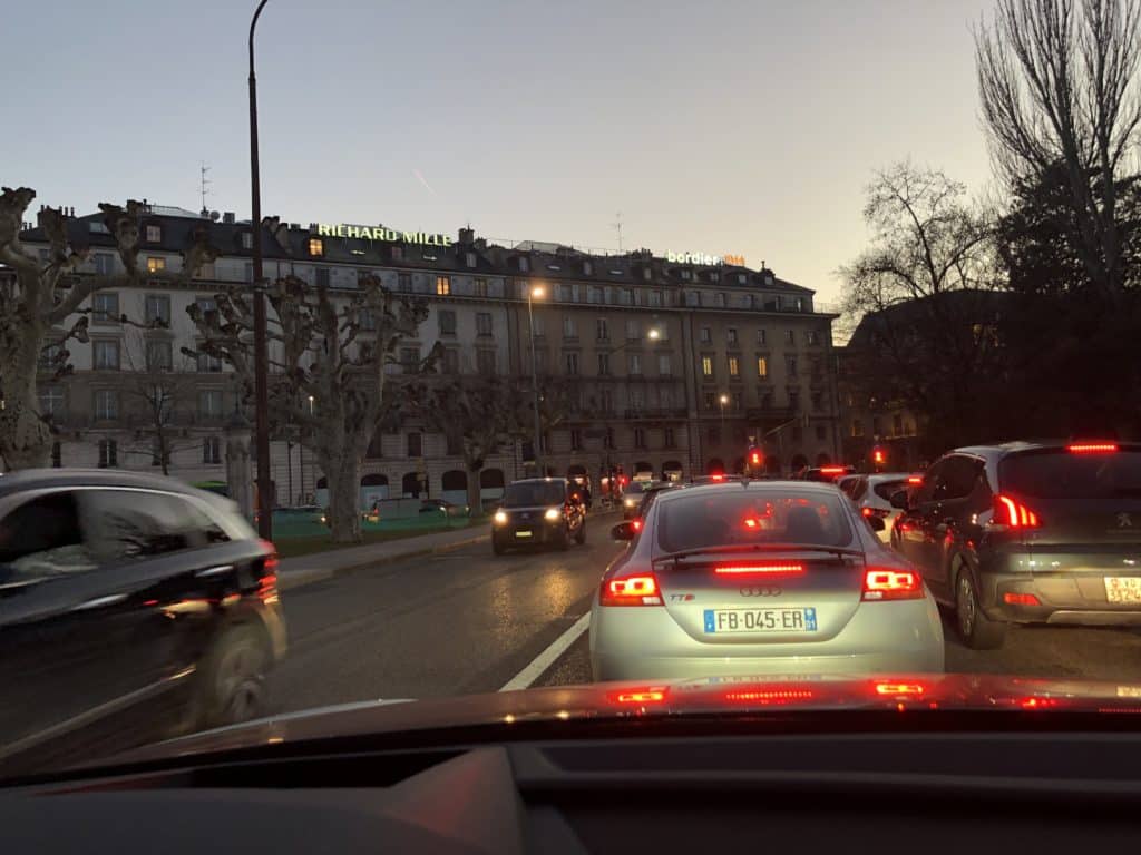 Photographie nocturne de l’enseigne lumineuse Richard Mille sur la façade d’un bâtiment élégant au quai Général-Guisan à Genève, avec les reflets des lumières sur la rue et une atmosphère urbaine raffinée.