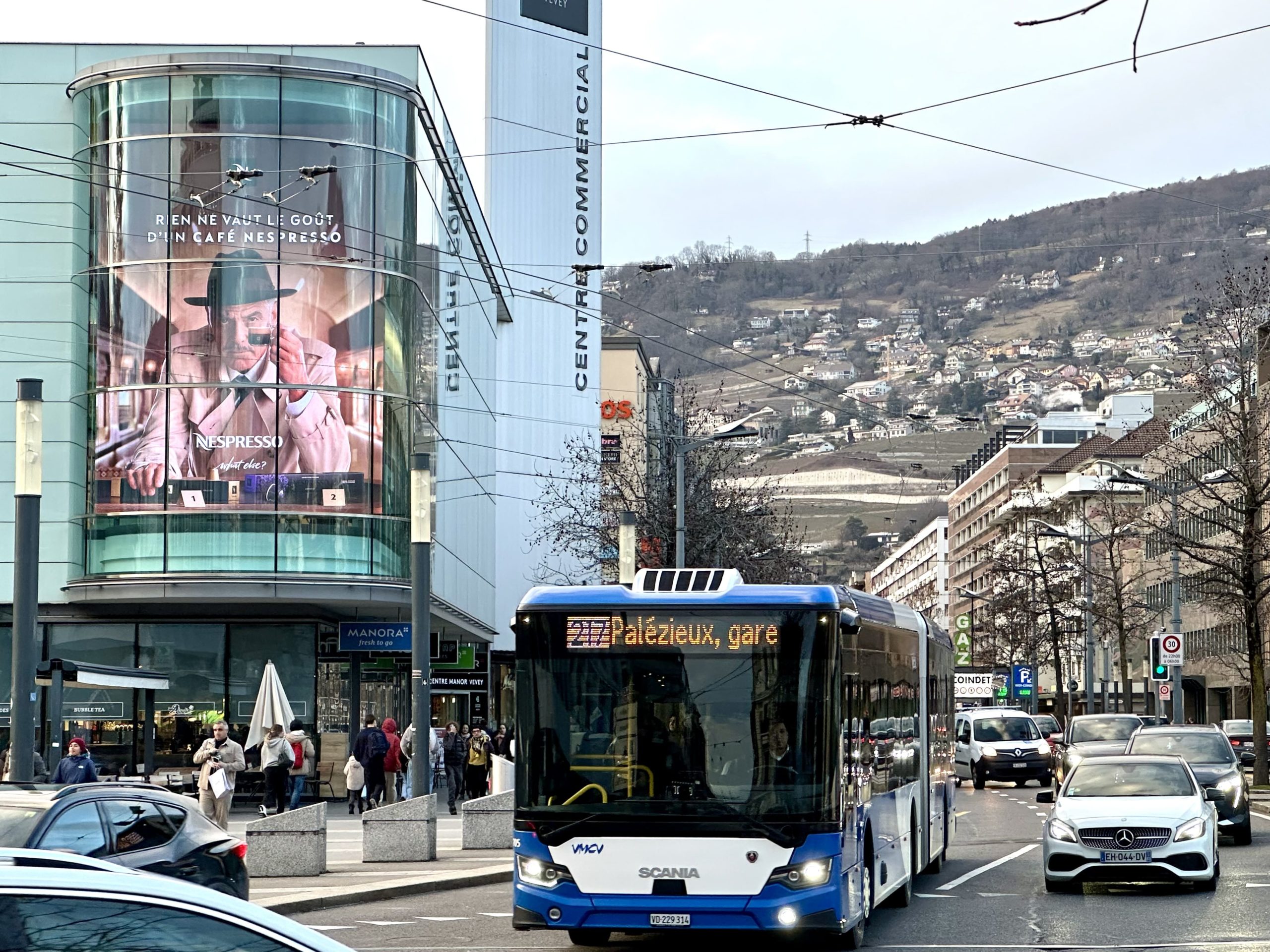 Grand mégaposter affiché sur la façade du magasin Manor au centre-ville de Vevey, visible depuis la rue et offrant une exposition maximale aux passants.