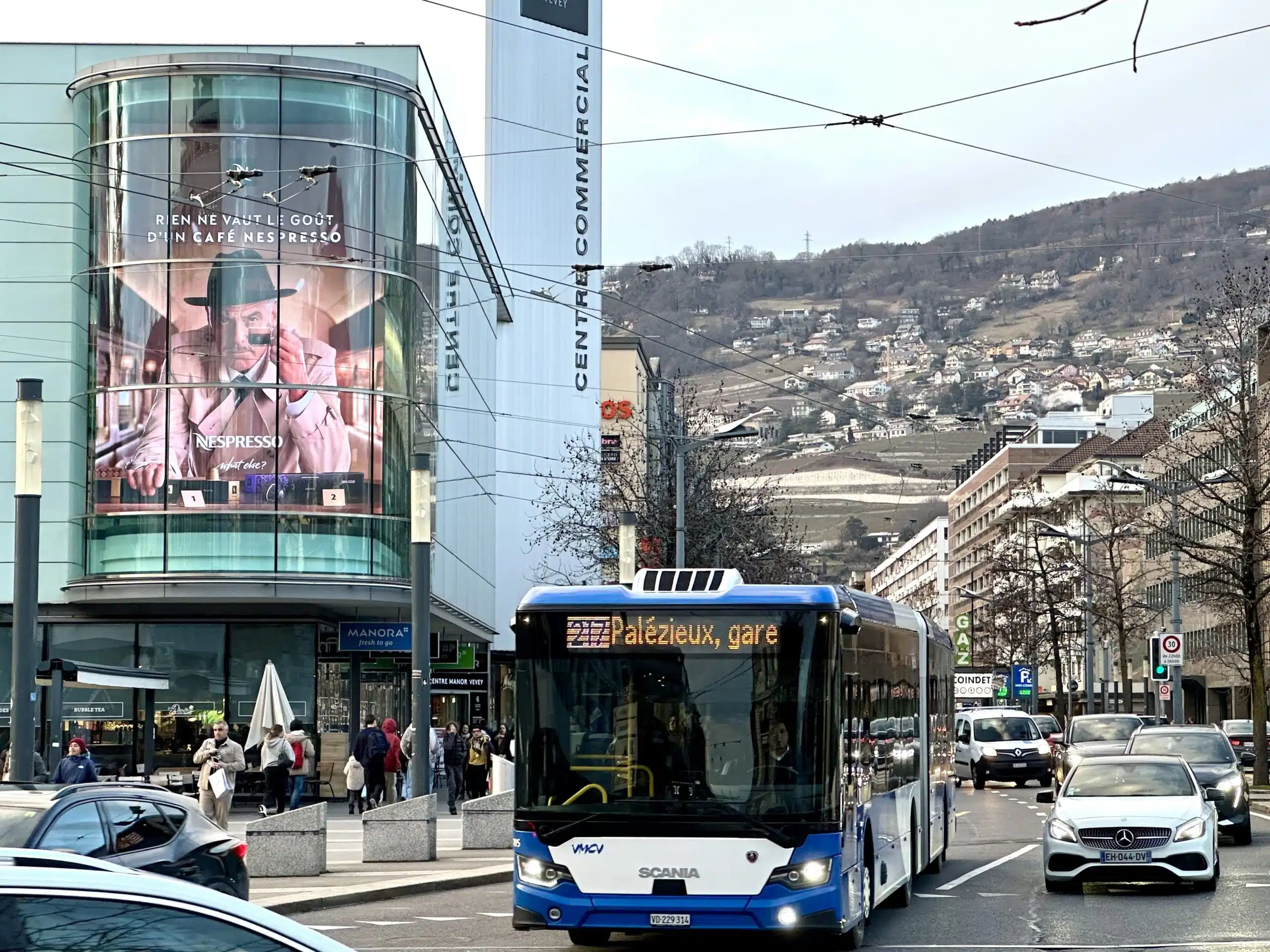 Grand mégaposter affiché sur la façade du magasin Manor au centre-ville de Vevey, visible depuis la rue et offrant une exposition maximale aux passants.