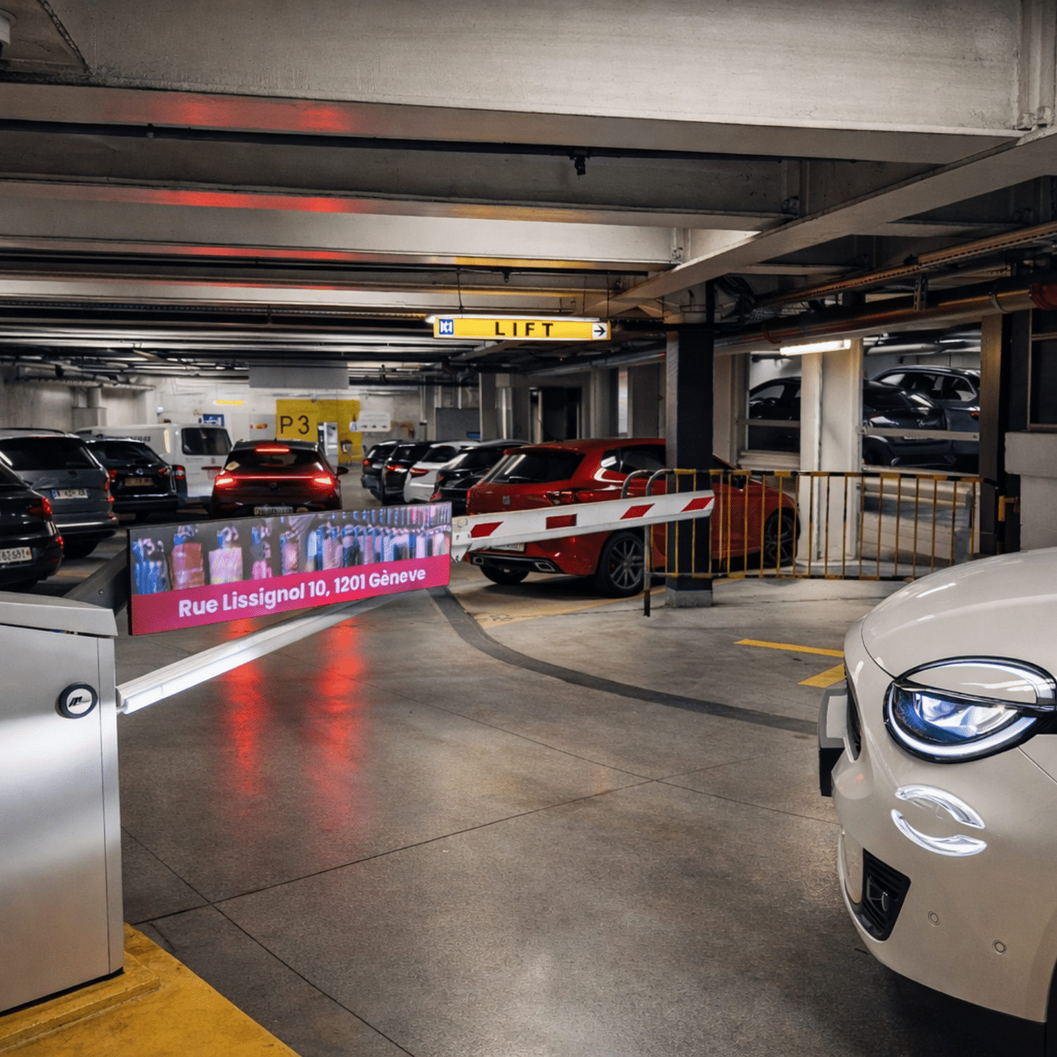Barrière de parking équipée d’un écran LED diffusant la publicité Cuvées du Terroir dans le parking souterrain de Manor Genève, avec véhicules stationnés et signalétique intérieure visible.